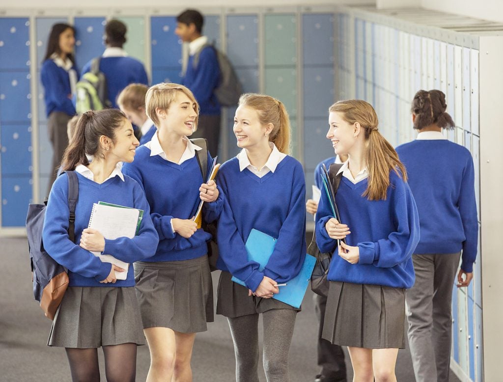 Cheerful female students wearing blue school uniforms walking in locker room